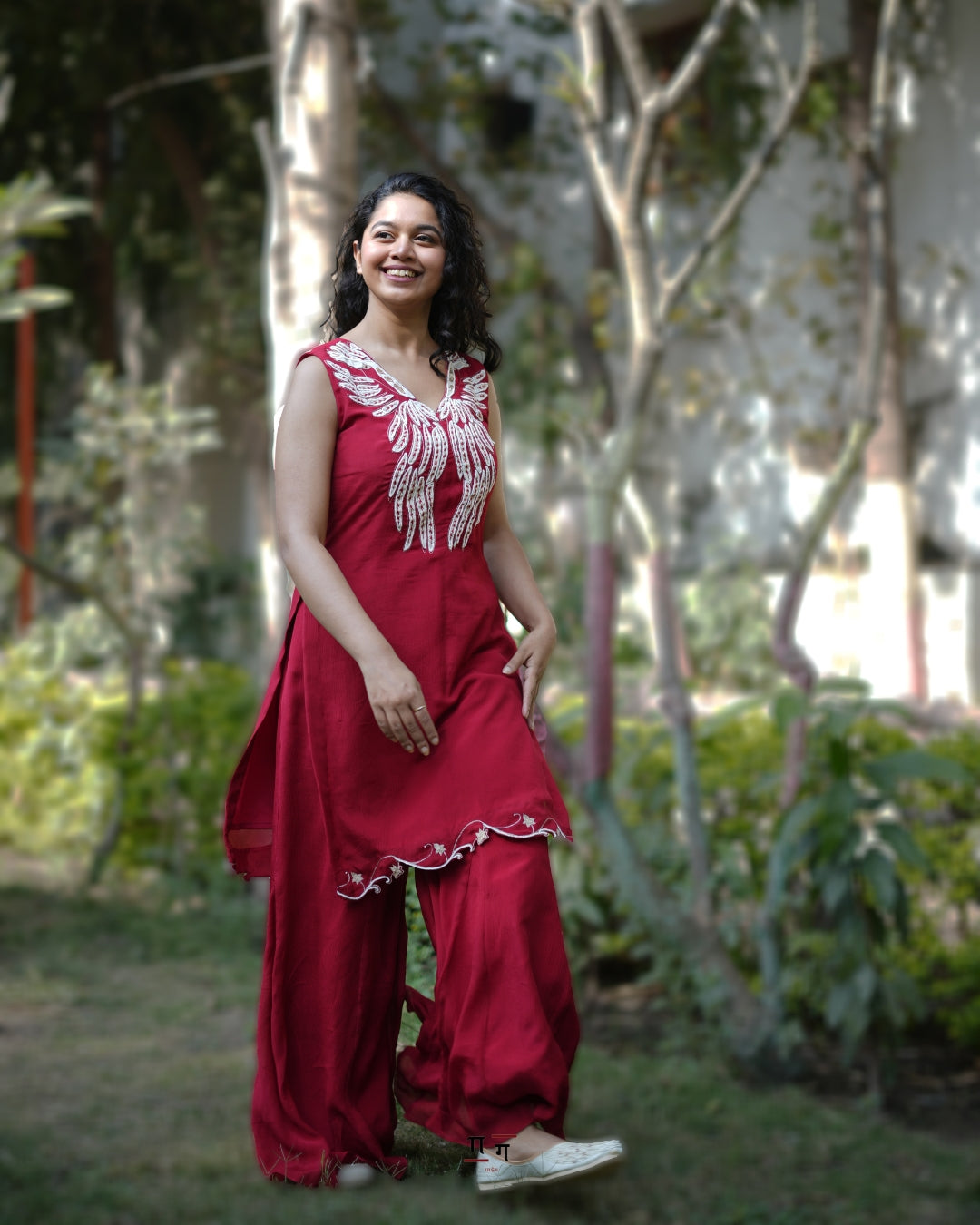 Woman in a red traditional outfit standing outdoors with trees in the background