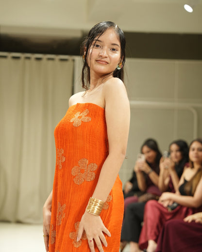 Woman in an orange dress with floral patterns on a fashion show runway.