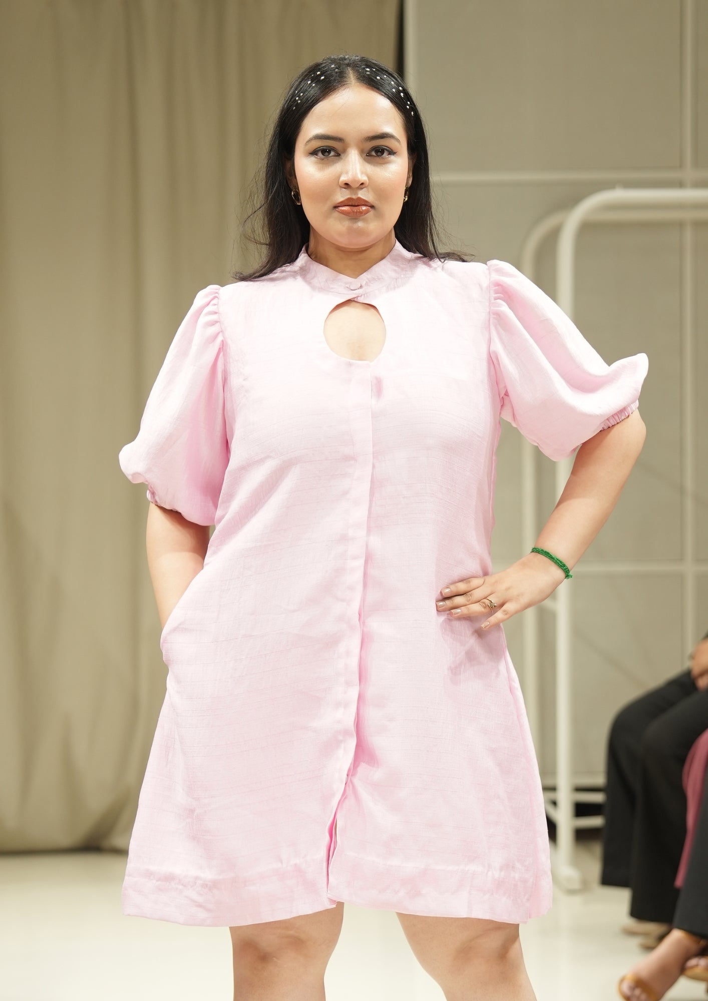 Woman wearing a pink dress with a cutout design on a neutral background