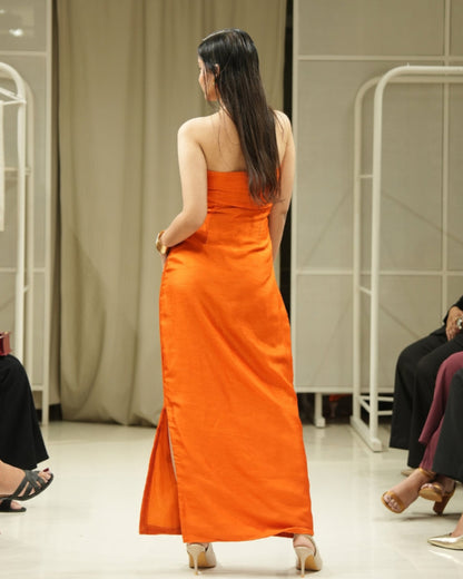 Model in an orange dress walking on a catwalk with an audience taking photos.