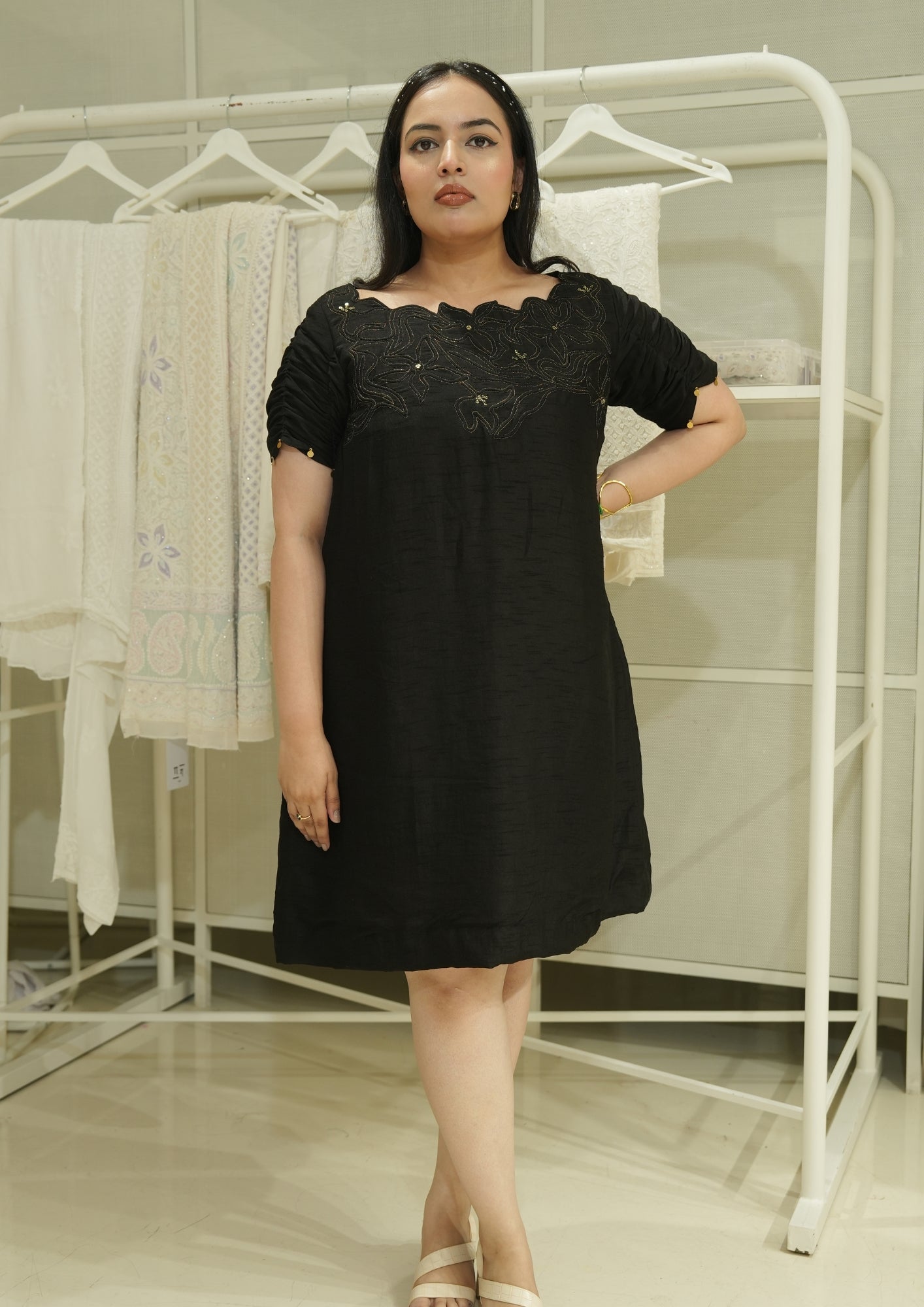 Woman wearing a black dress standing in front of a clothing rack.