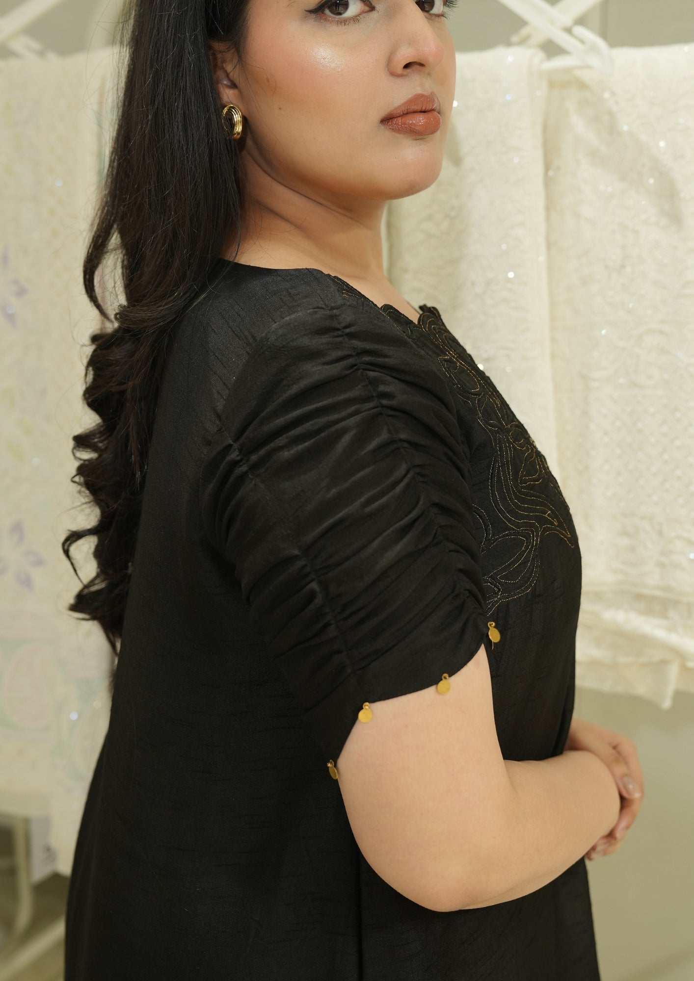 Woman wearing a black outfit with gold accents against a white textured background