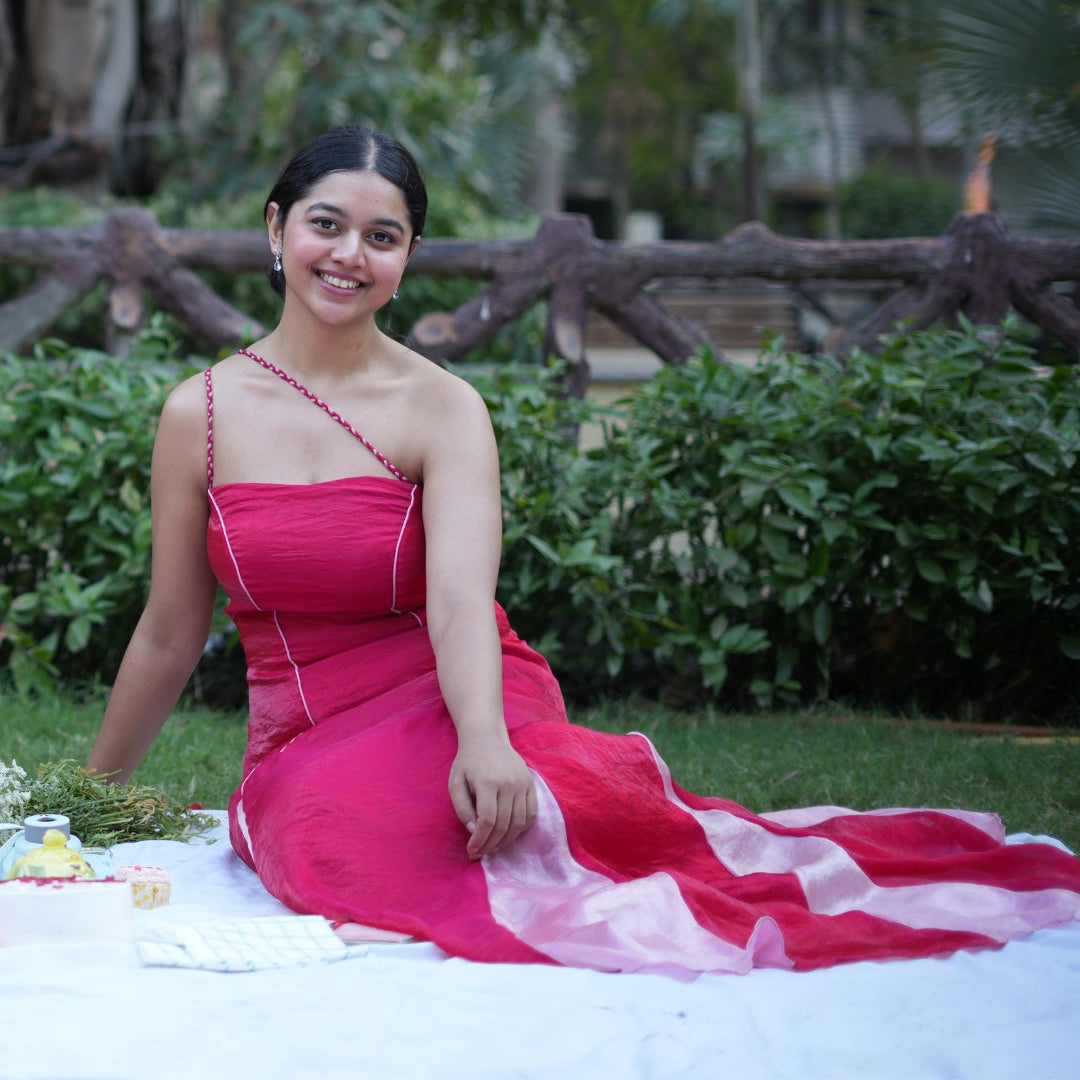 Woman in a red dress sitting on a blanket outdoors with greenery in the background