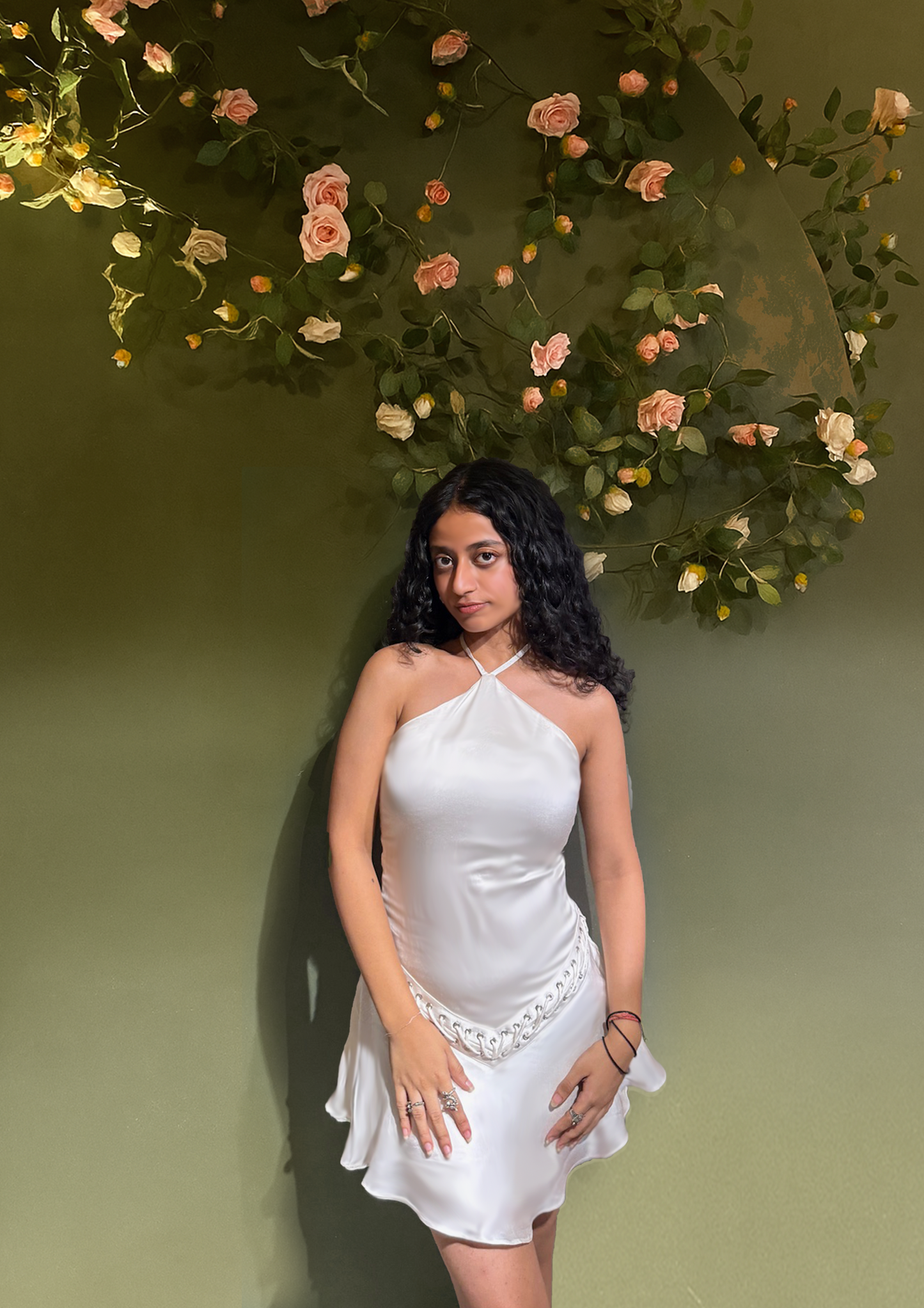Woman in a white dress standing against a floral and green leafy background